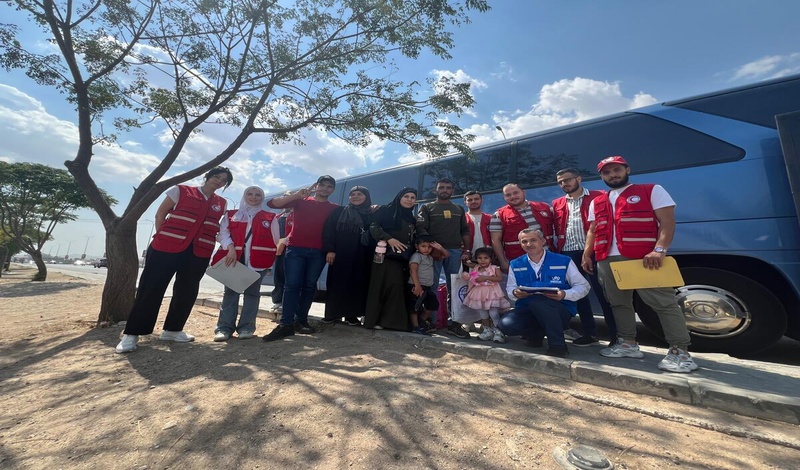 A crowd of people gathers behind several trucks filled with passengers