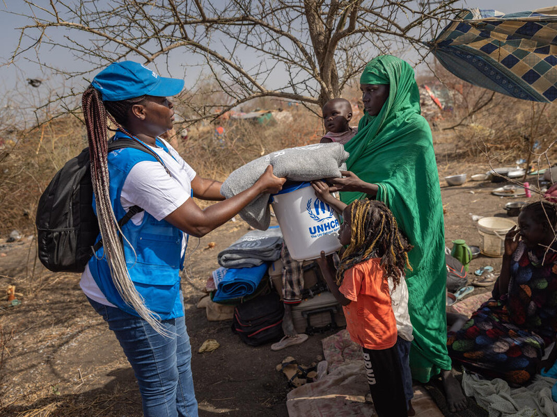 A woman receives a blanket and other supplies from a UNHCR staff member.