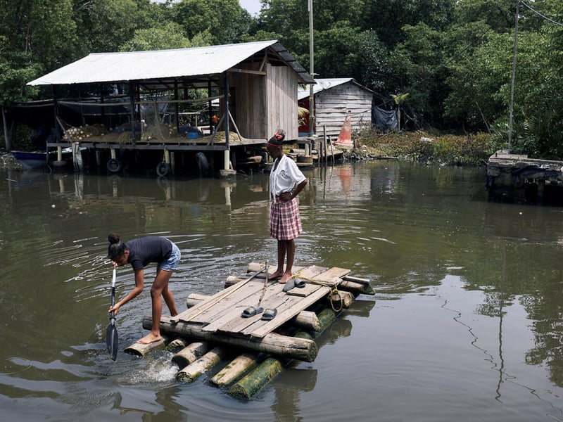 Two girls paddle across mangrove canal on a makeshift wooden raft