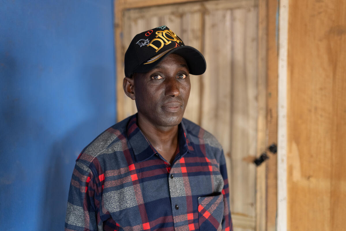 Un homme portant une casquette de base-ball et une chemise en flanelle regarde fixement la caméra.