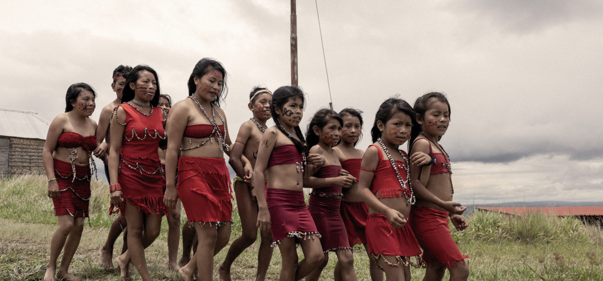 A group of young indigenous people wearing traditional dress walk together near their village