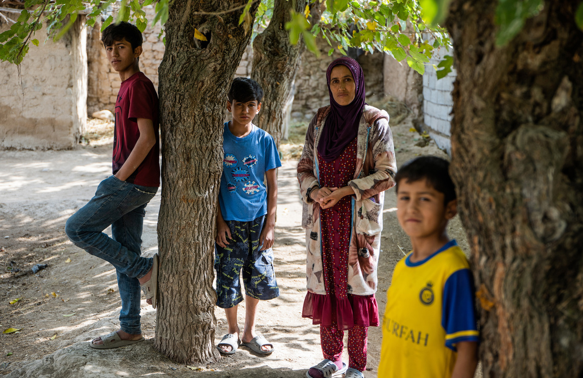 Une femme se tient au milieu de quelques arbres avec trois garçons d'âges différents.