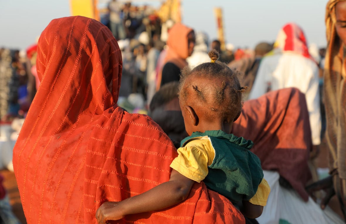 A woman in orange pictured from behind, carrying her child.