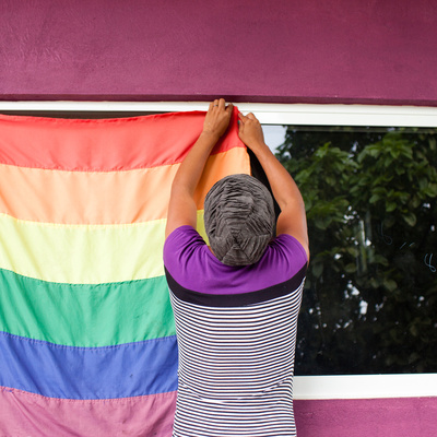 A person hangs a rainbow flag to a window.