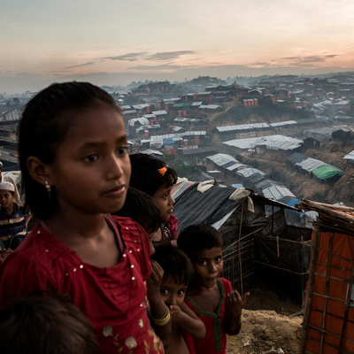 Young Rohingya refugees on a hillside at dusk overlooking a sprawling array of shelters.