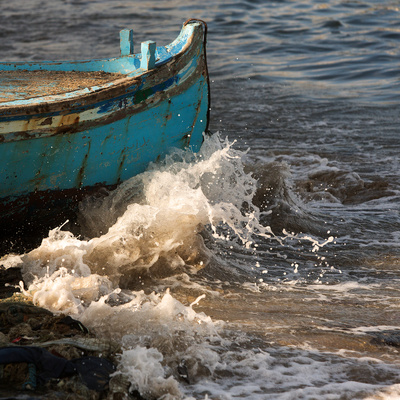 Waves crash against the bow of a teal fishing boat 