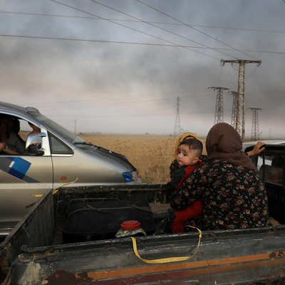 Syria. A woman with a baby sits at a back of a truck as they flee Ras al Ain town