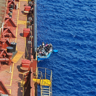 Malta. Migrants sit in a boat alongside the Maersk Etienne tanker