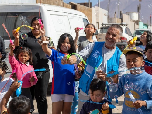 Osvaldo Laport blows bubbles with a group of smiling refugee, migrant and host community children and adults.