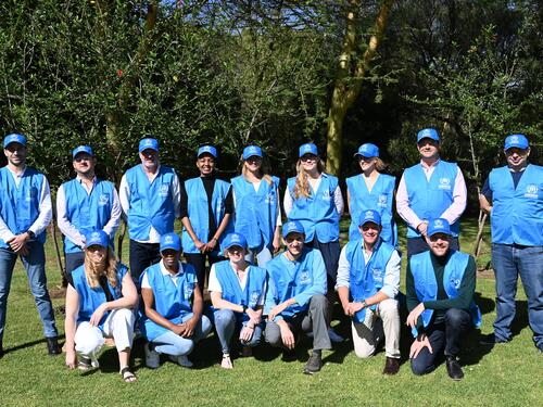 A group of about 15 people wearing blue UNHCR vests smile for the camera