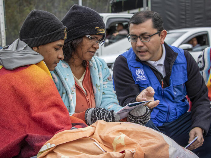 A UNHCR staff member explains a pamphlet to a man and a woman.