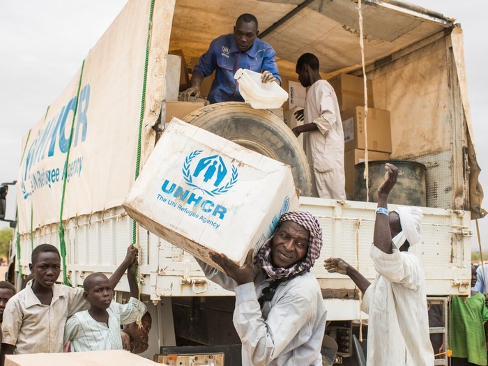 UNHCR staff unload boxes of emergency supplies from a truck in a refugee camp. 