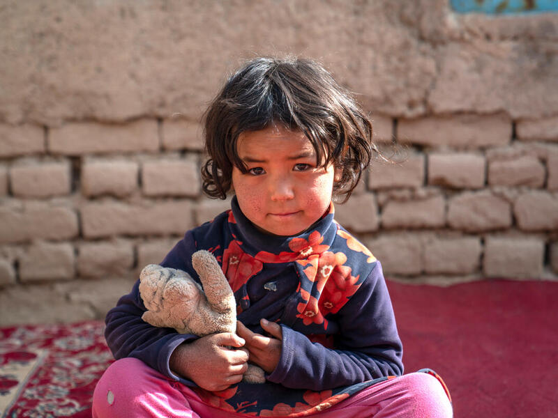 A young internally displaced girl in Afghanistan cuddles a soft toy.