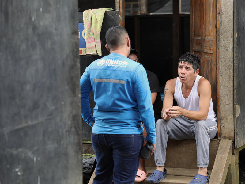 Owar, who fled Venezuela in search of a better life, sits on steps outside a shelter speaks with a UNHCR staff member.