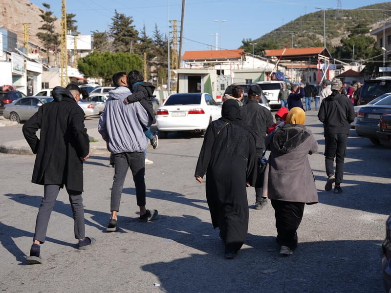 Groups of people pictured walking, from behind, next to parked cars