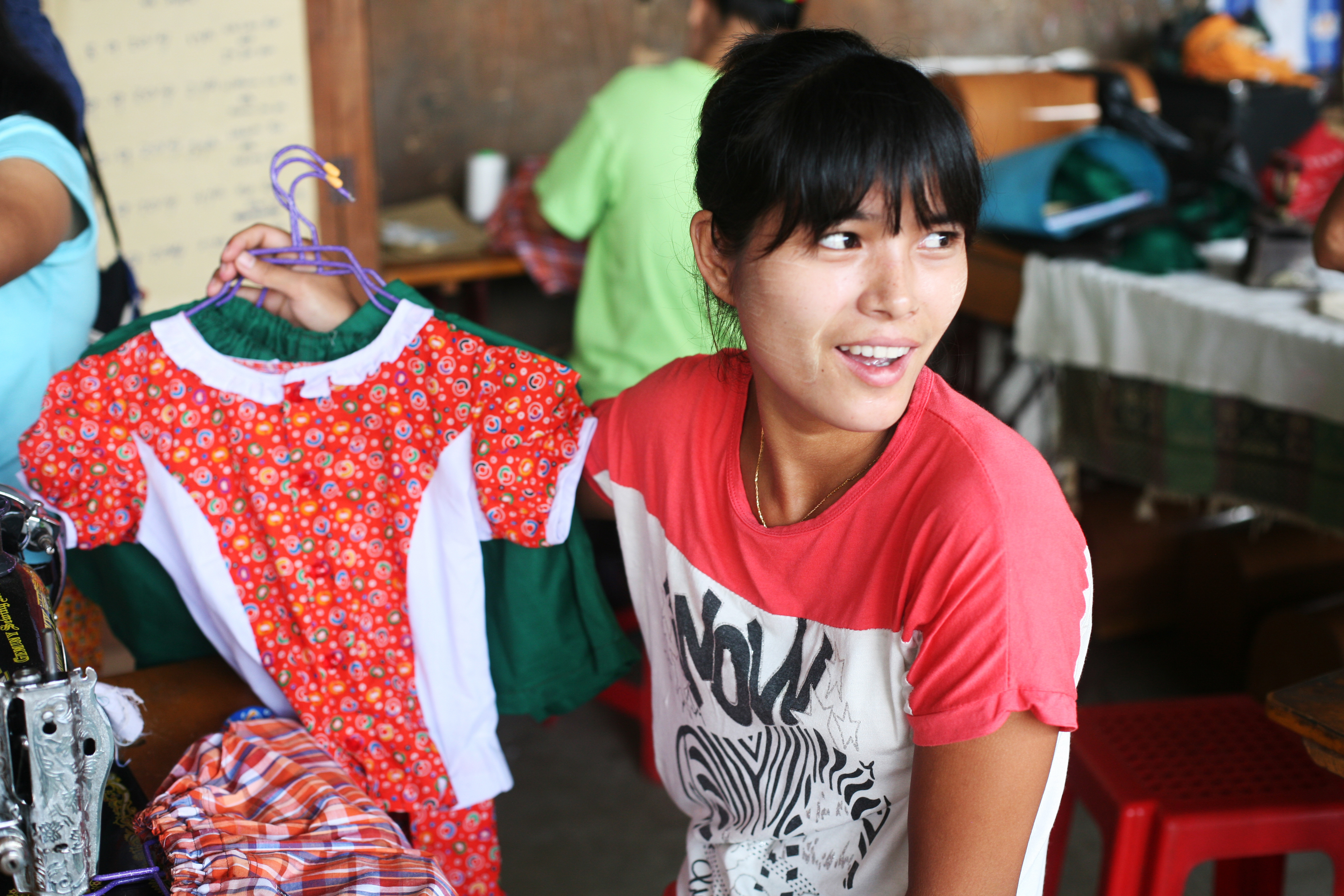 One of the tailoring trainees proudly holds up children's clothing that she has made.