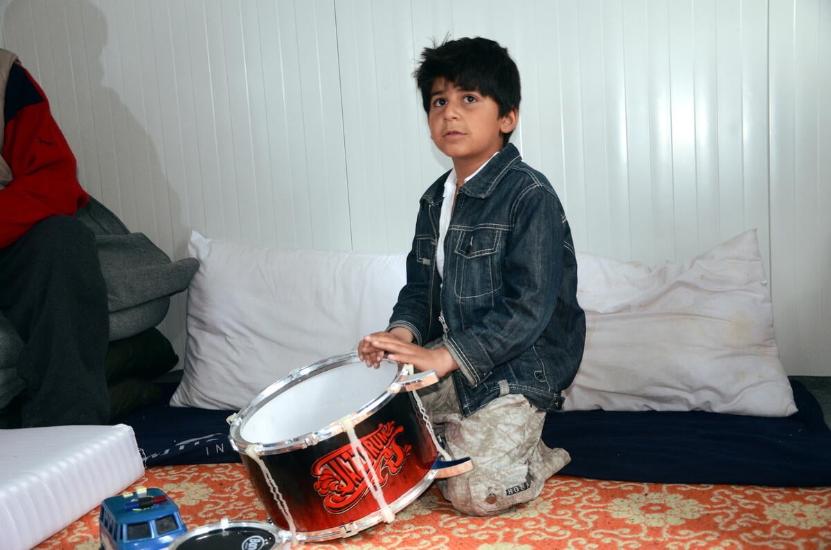Afghan boy Farzad that stopped taliking after separation from his mother, playing on drums in a UNHCR prefab in Karatepe site