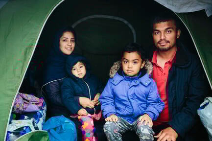 A small family of asylum-seekers smile from inside their tent at an improvised camp in Greece. 