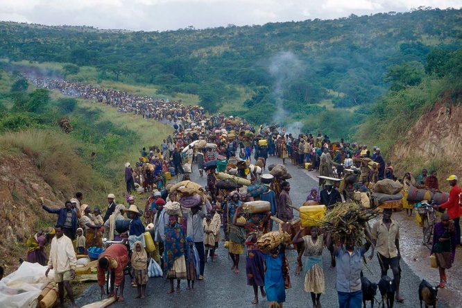A large group of Rwandan refugees walk on a road through the country side