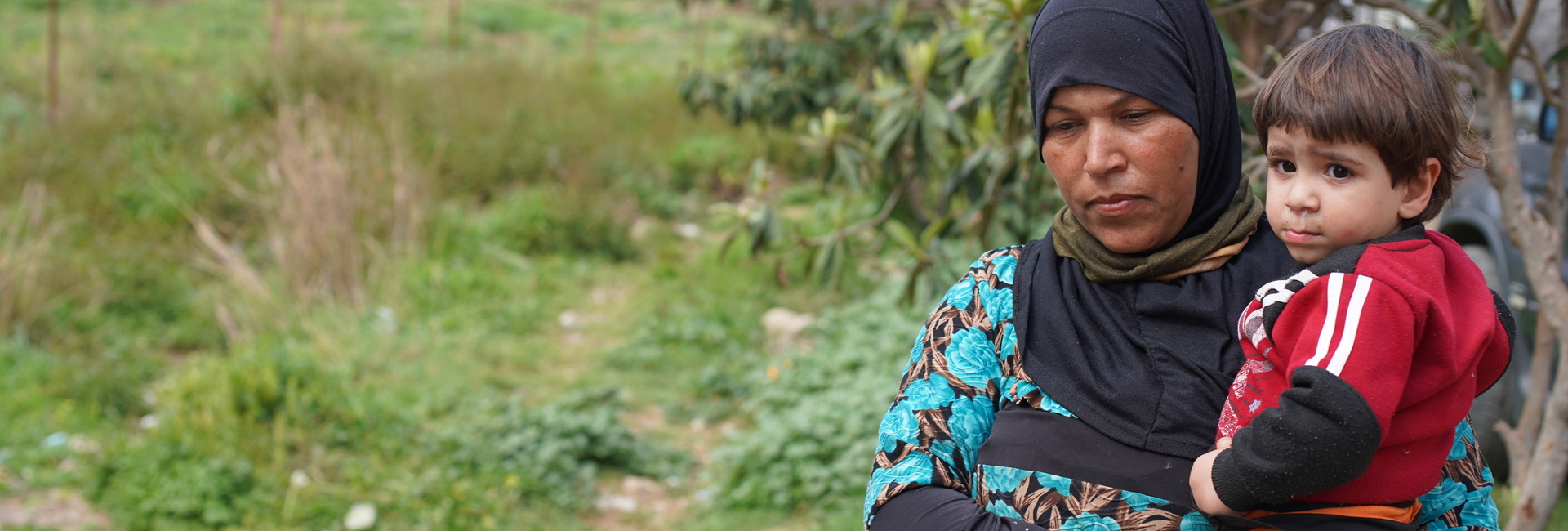 A Syrian woman holds her young nephew in a field near their home