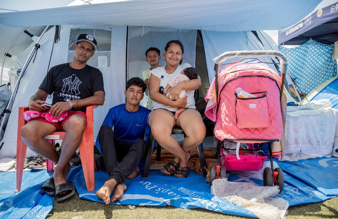 A family sits outside the entrance to a tent