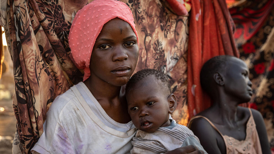 A young woman from South Sudan holds her one-year-old sister.