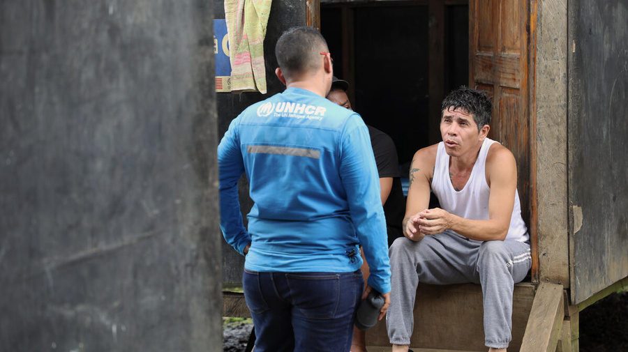 Owar, who fled Venezuela in search of a better life, sits on steps outside a shelter speaks with a UNHCR staff member.