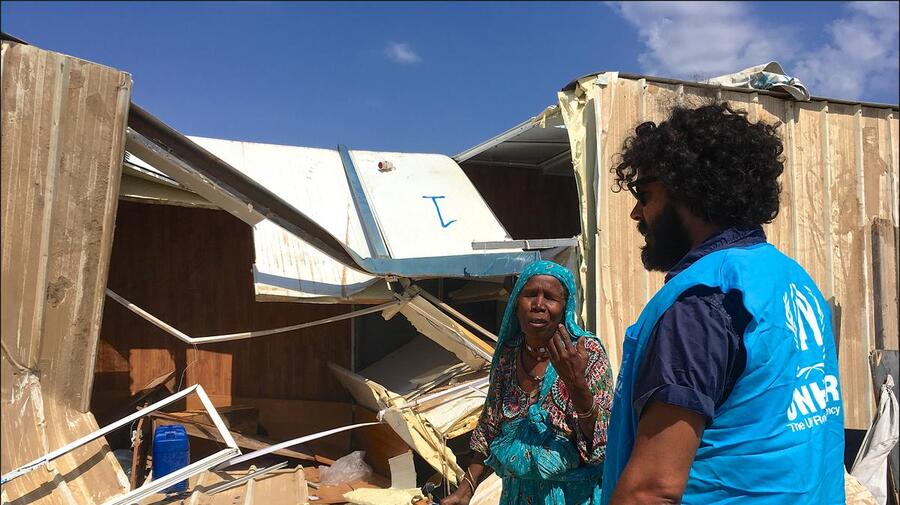 A displaced woman speaks to a man wearing a blue UNHCR vest in front of her collapsed shelter in Triq al Matar settlement in Libya.