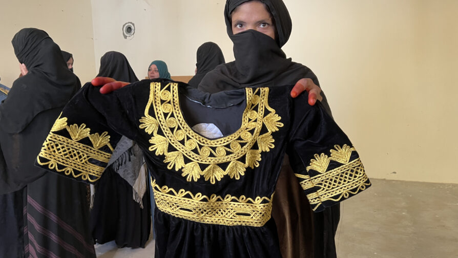 En af de kvinder, der har modtaget undervisning i at sy gennem UNHCR-projektet, viser her noget af det tøj, som hun har lavet. © UNHCR/Caroline Gluck