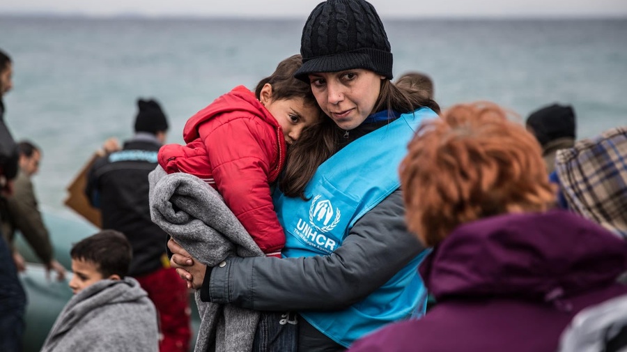 A UNHCR staff member holds a young refugee child in a blanket.