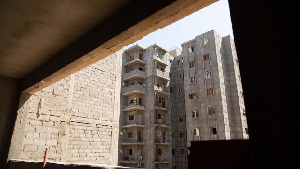 Een raam zonder glaswerk in het appartement van Hanan kijkt uit over andere onafgemaakte gebouwen die momenteel onderdak bieden aan meer dan 100 ontheemde Libische families. © UNHCR/Mohamed Alalem