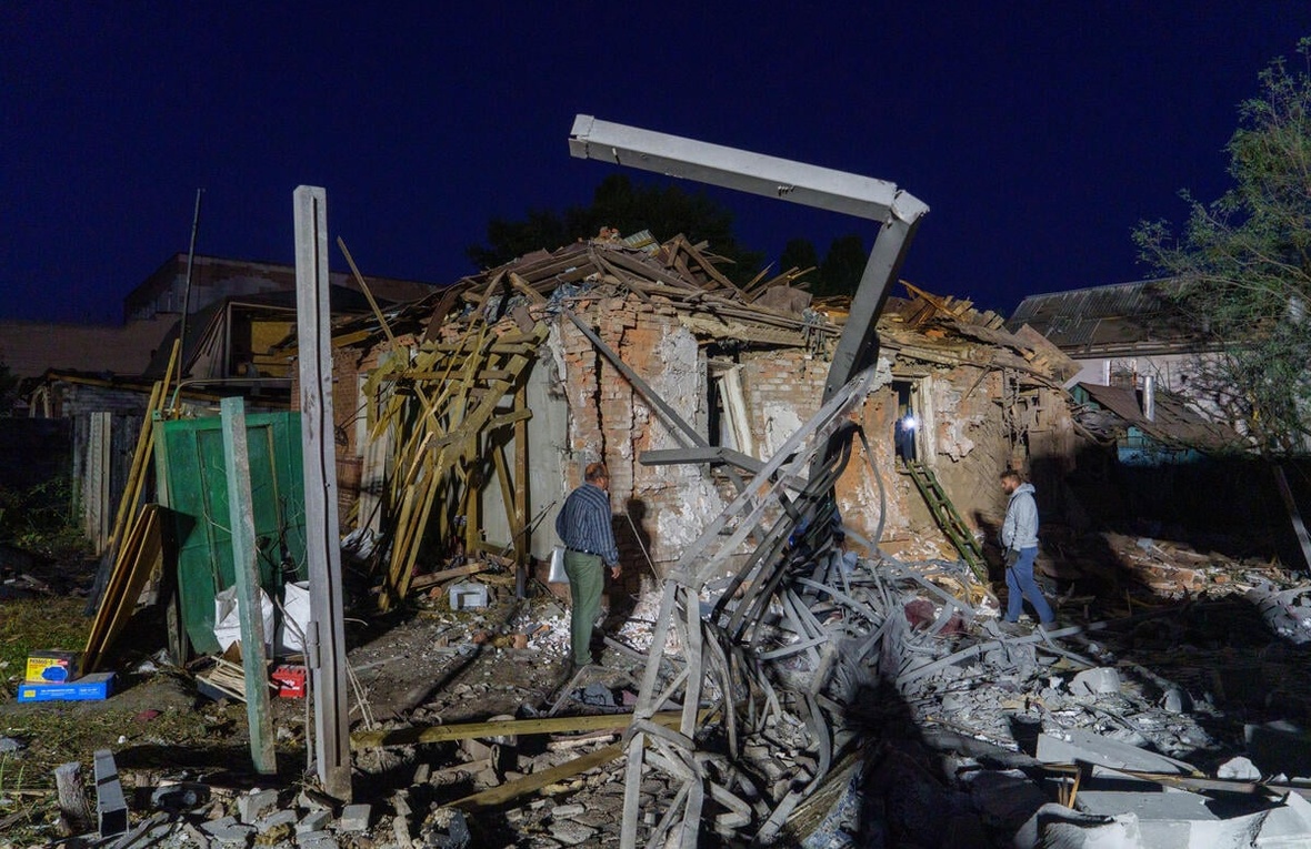 Two people assess damaged and collapsed buildings.