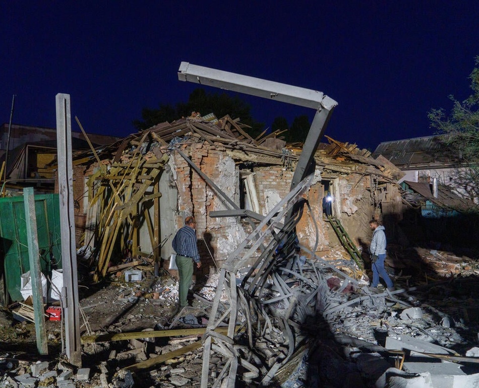Two people assess damaged and collapsed buildings.
