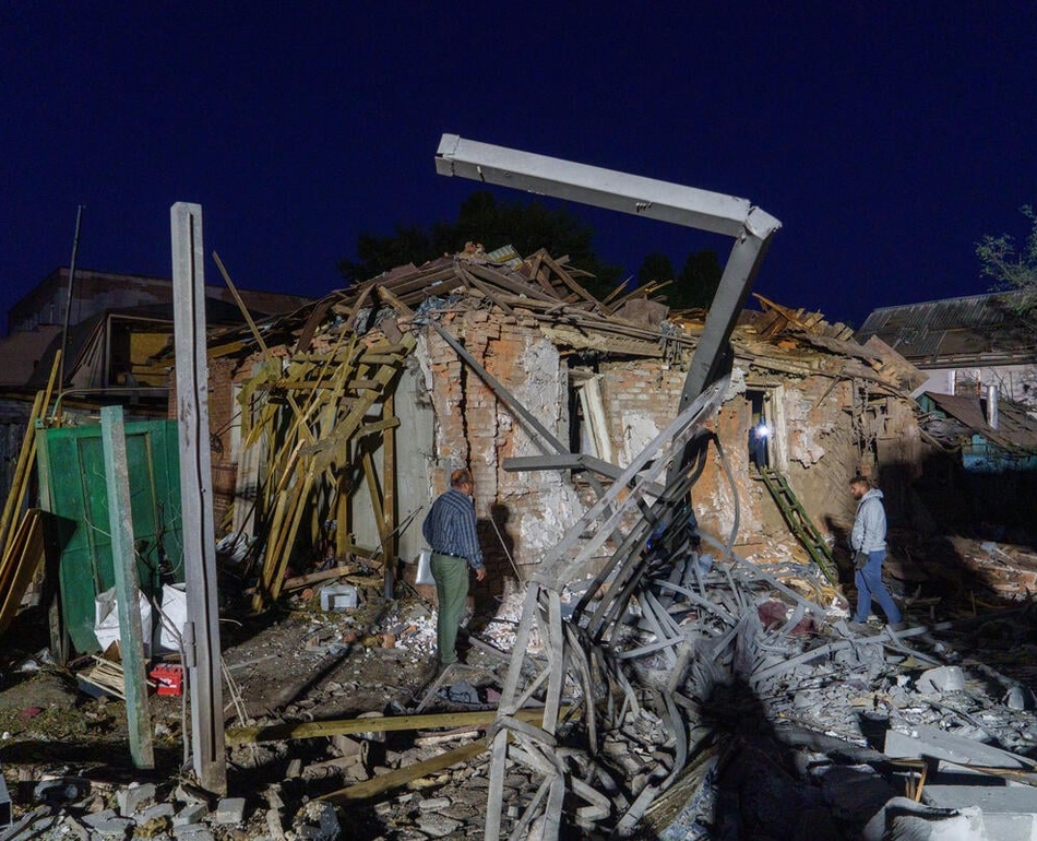 Two people assess damaged and collapsed buildings.