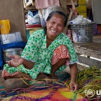 Ina Biri happily shows how she transforms fresh pandan leaves into a beautifully woven mat, crafting this traditional piece right in the comfort of her home.