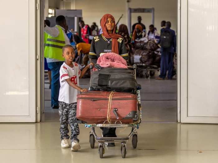 Burundian sister and brother walk their luggage on a trolley through an airport