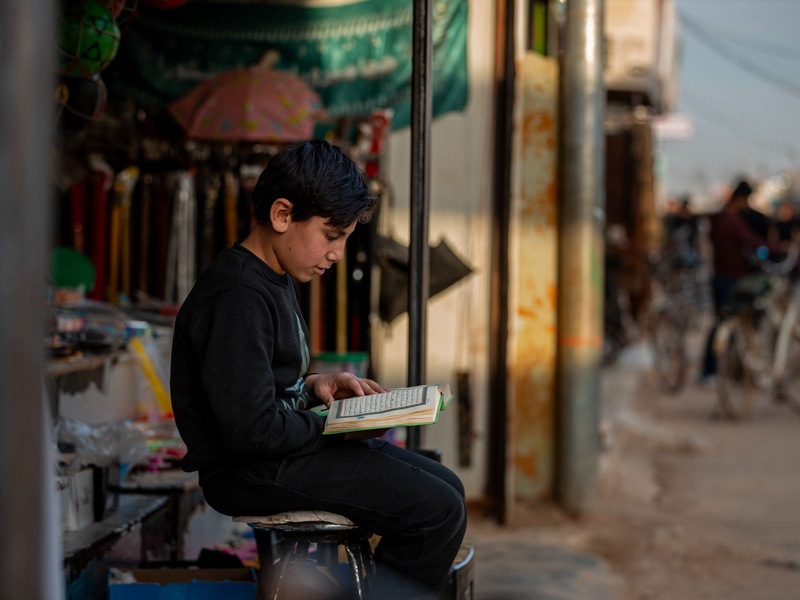 A syria refugee child reads the Quran in front of his shelter at Zaatari camp, Jordan