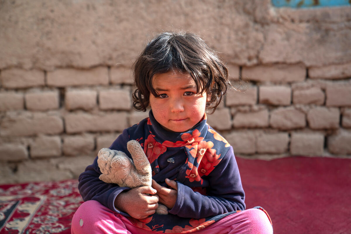 A young internally displaced girl in Afghanistan cuddles a soft toy.