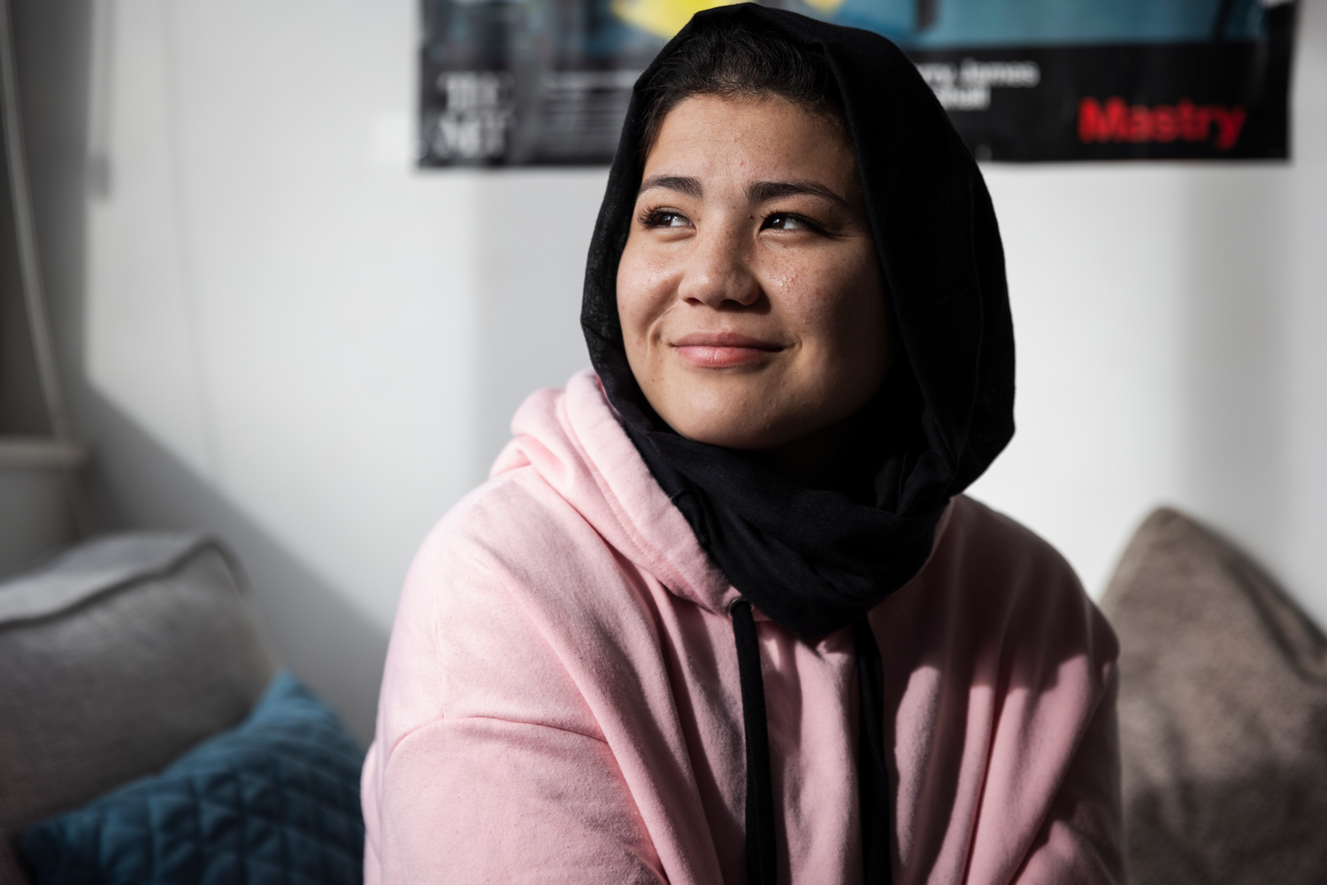A young smiling woman in a pink hoodie and a black head scarf.