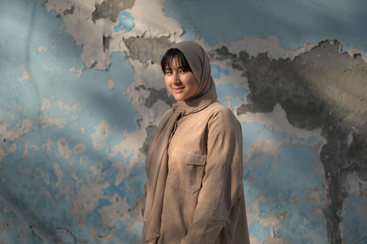 Afghan refugee woman stands in front of a blue wall.
