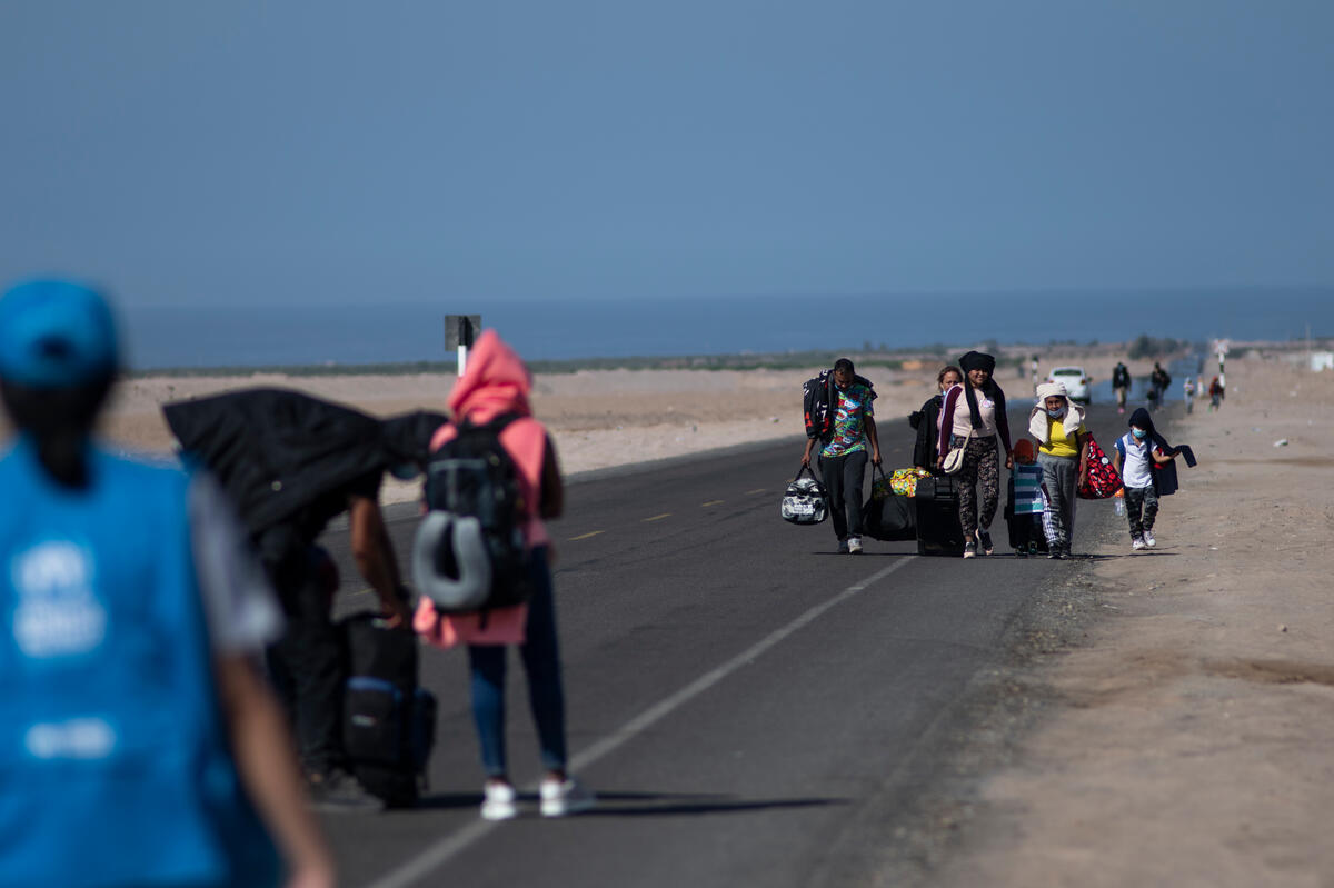 Refugees walk on a highway, with the sea in the background