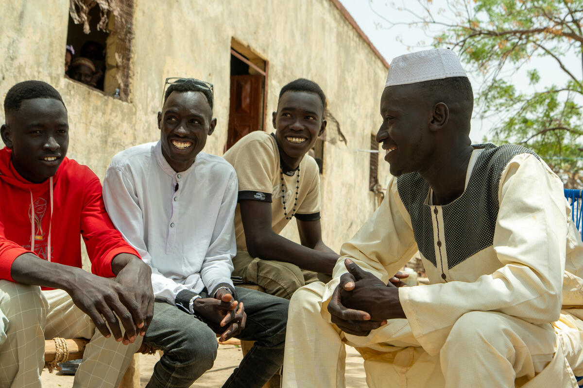 Four young men sit outside a building chatting.