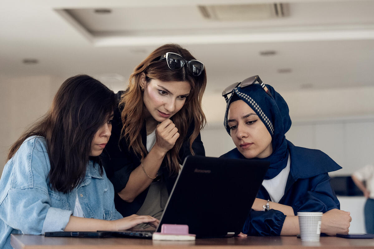 Three women in a work meeting look at the screen of a computer