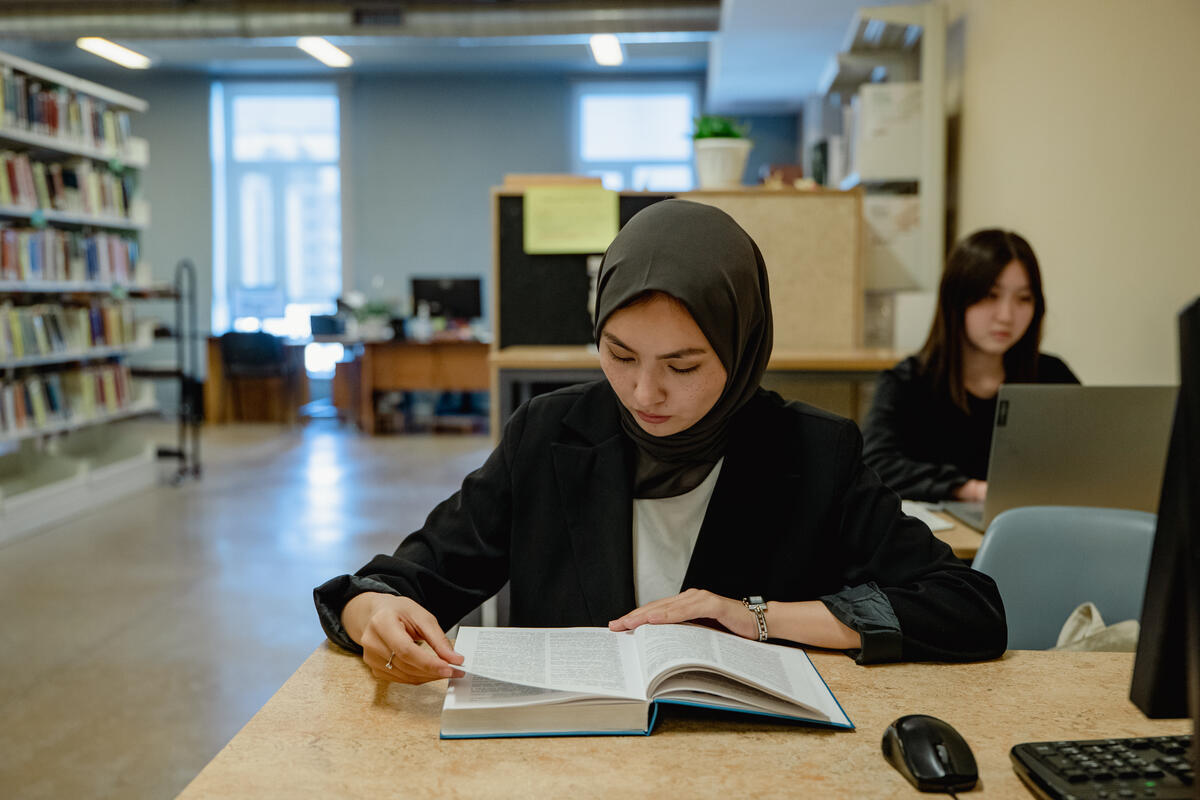 A young woman sits at a table reading a book in a library.