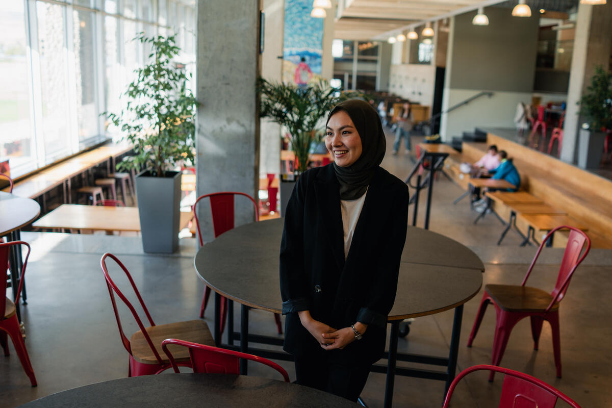 A young smiling woman leans against a table in a university cafe.