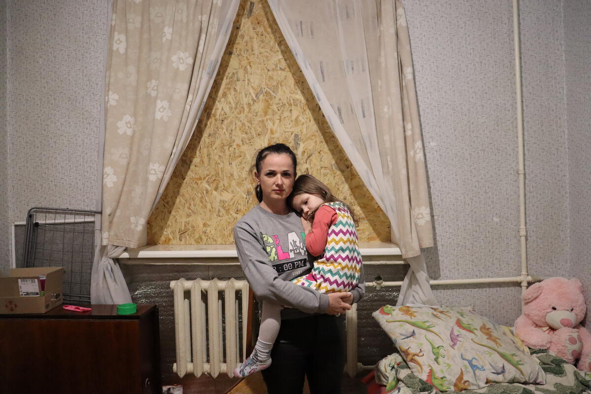 A mother holds her young daughter in front of a boarded-up window in her child's bedroom.