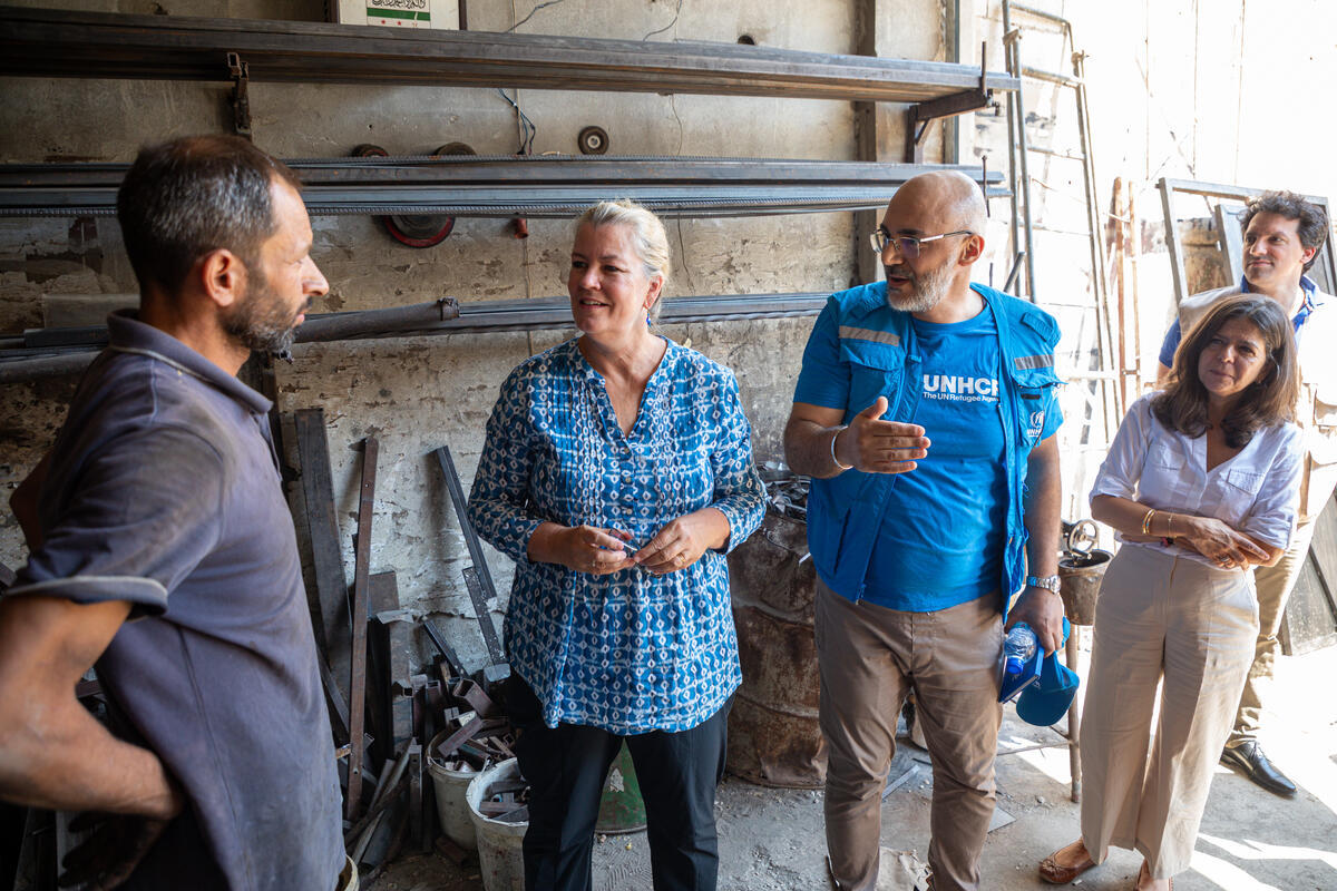 A group of four people stand talking inside the open doorway of a metal workshop
