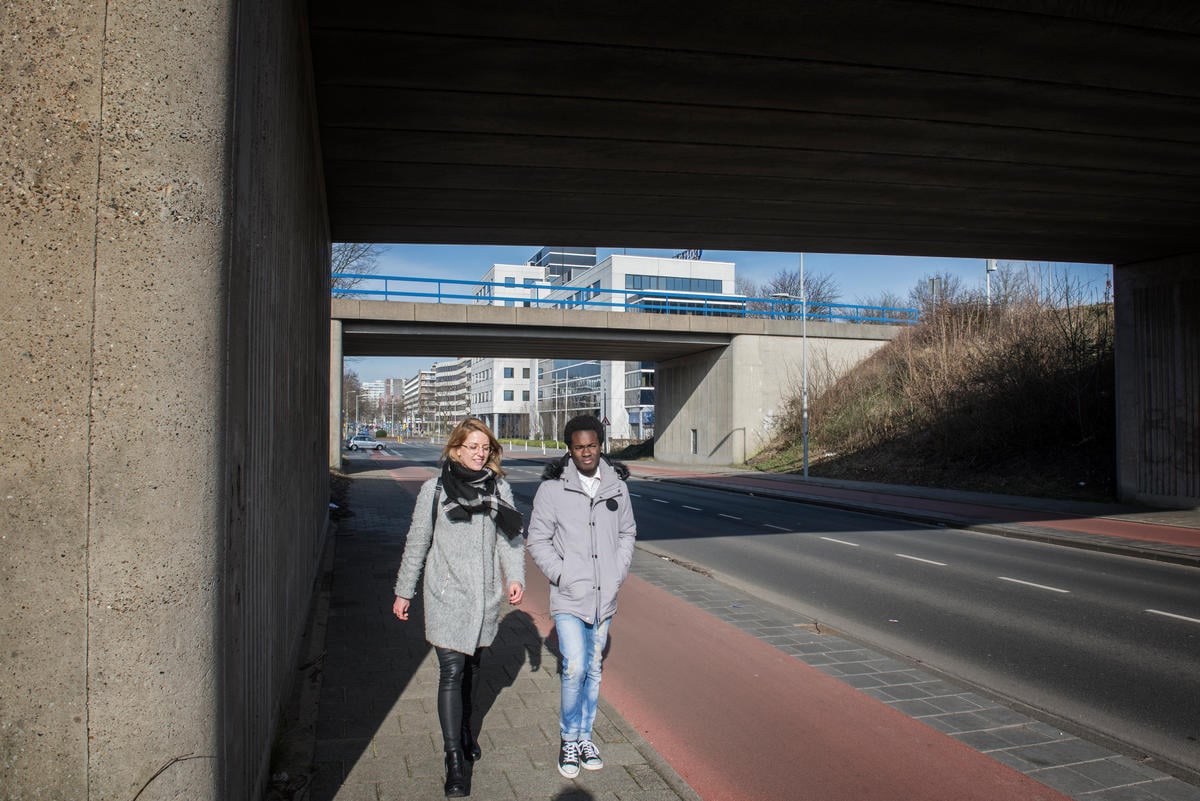 Two friends in jackets walking outside under a bridge