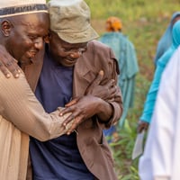 الزعيم سوديا يعانق أحد اللاجئين المقيمين في قرية غادو-بادزيري في حقلٍ قرب القرية.