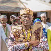 A man in colourful robes with his arms crossed stands in front of a group of people